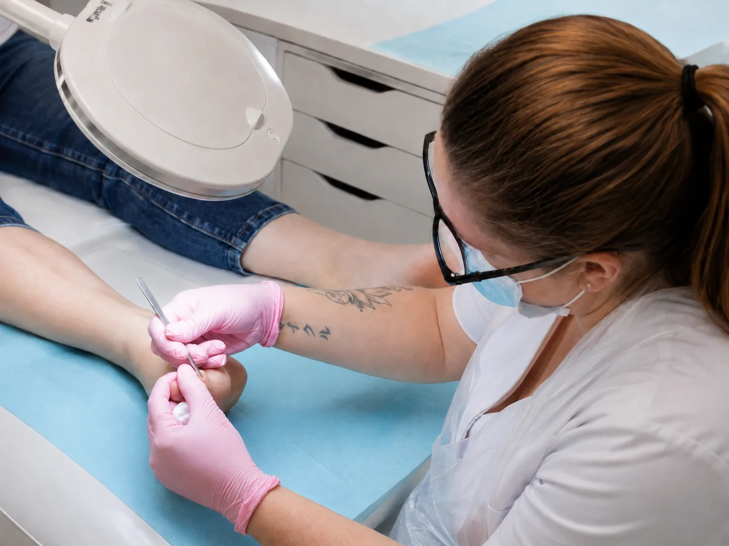 Medisch pedicure behandelt de tenen van een cliënt met handschoenen en een vergrootlamp.