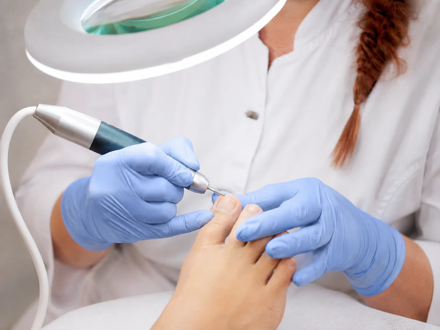 Close-up van een pedicurebehandeling waarbij de teennagel met een elektrisch instrument wordt verzorgd.